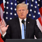 Donald Trump giving a speech with American flags behind.