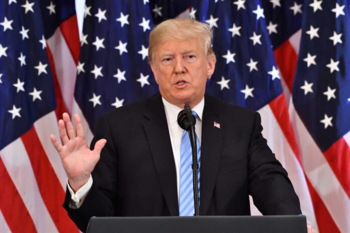 Donald Trump giving a speech with American flags behind.