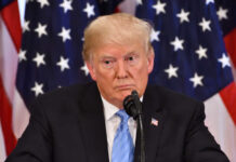 Donald Trump speaking with American flags in background.