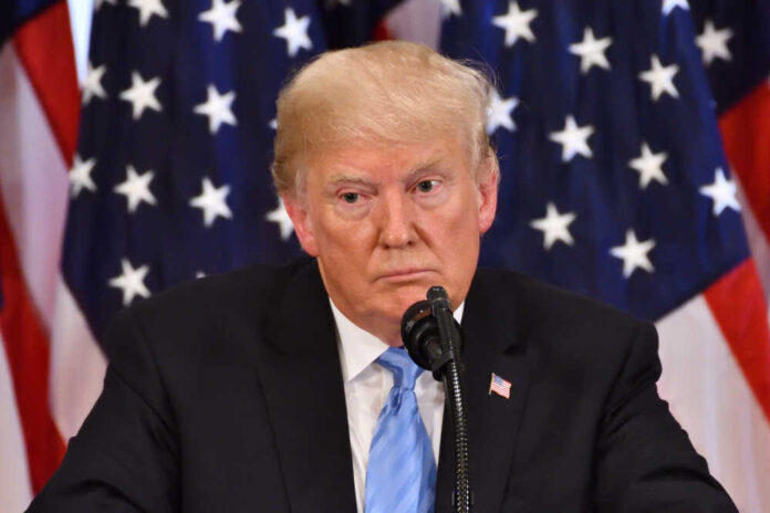 Donald Trump speaking with American flags in background.