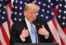 Donald Trump speaking in front of multiple American flags.