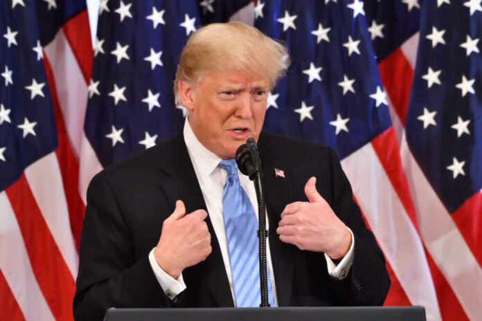 Donald Trump speaking in front of multiple American flags.