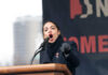 Alexandria Ocasio-Cortez passionately speaking at a podium outside.