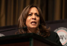 A woman speaking at a podium, looking serious.