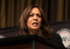 A woman speaking at a podium, looking serious.