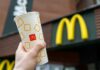 Hand holding McDonald's cup in front of restaurant sign.