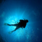 Scuba diver underwater with sun rays filtering through.