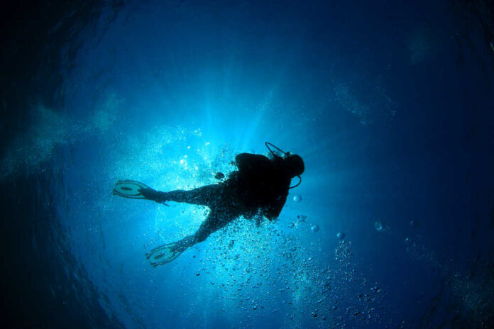 Scuba diver underwater with sun rays filtering through.