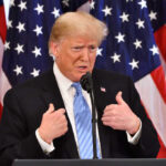 Donald Trump speaking in front of multiple American flags.