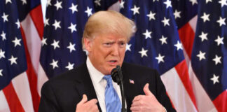 Donald Trump speaking in front of multiple American flags.