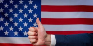 Thumbs up in front of American flag background.