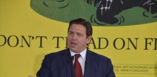 Ron DeSantis speaking in front of yellow Don't Tread sign.