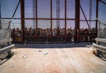 People standing behind a fence on a dusty path.