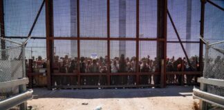 People standing behind a fence on a dusty path.