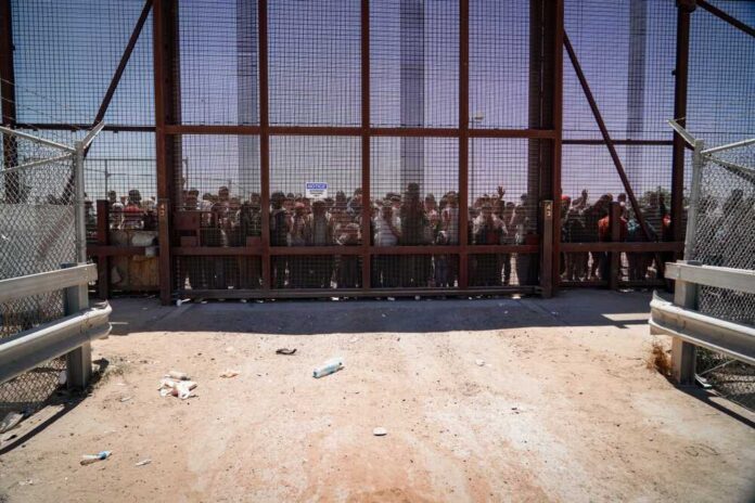 People standing behind a fence on a dusty path.