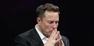 Elon Musk in a suit deep in thought, black background.