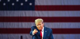 Donald Trump in front of American flag pointing toward camera.