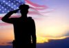 Silhouette saluting soldier, American flag, sunset background.