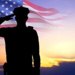 Silhouette saluting soldier, American flag, sunset background.