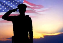 Silhouette saluting soldier, American flag, sunset background.