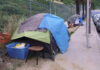 Homeless encampment with tents and belongings on a sidewalk.