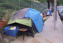 Homeless encampment with tents and belongings on a sidewalk.