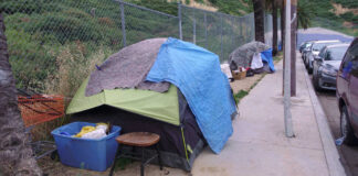 Homeless encampment with tents and belongings on a sidewalk.