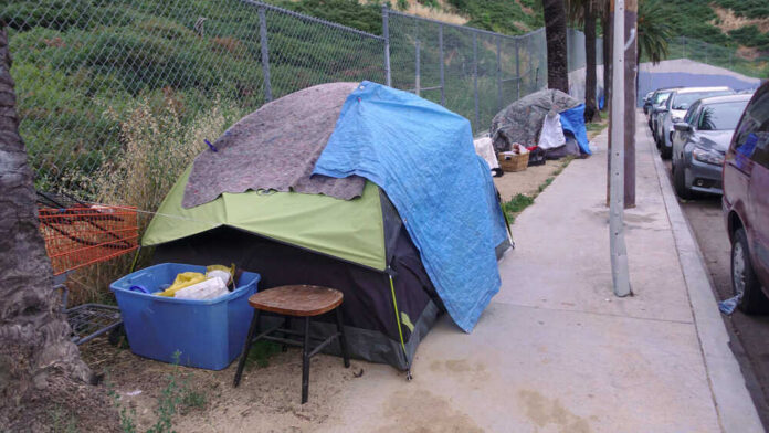 Homeless encampment with tents and belongings on a sidewalk.