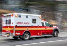 Red and white ambulance driving on a city street.