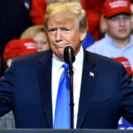 A man in a suit speaking at a rally.