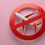 Airplane inside red prohibition sign on pink background.