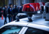 Police car roof with lights, officers in background.