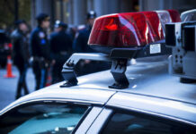 Police car roof with lights, officers in background.