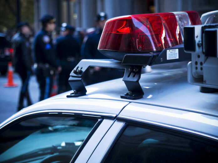 Police car roof with lights, officers in background.