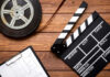 Film reel, clapperboard, and storyboard on wooden table.