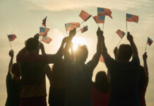 People holding and waving American flags at sunset sky