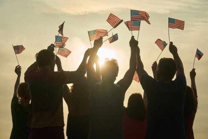 People holding and waving American flags at sunset sky