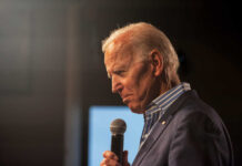 Man holding microphone, wearing suit, looking downward thoughtfully.