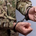 Person in military uniform handcuffed hands close up