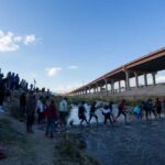 Migrants crossing river near bridge walkway at the US Mexico border