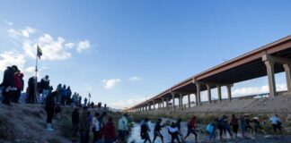 Migrants crossing river near bridge walkway at the US Mexico border