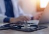 Stethoscope and tablet on desk, doctor using laptop.