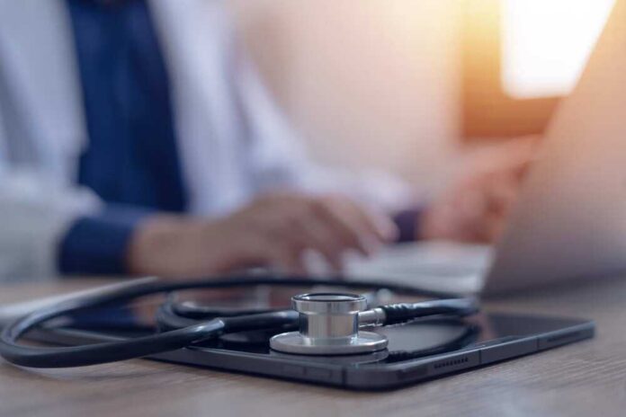 Stethoscope and tablet on desk, doctor using laptop.