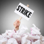 Hand holding strike sign amid crumpled paper pile