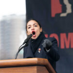 Alexandria Ocasio-Cortez passionately speaking at a podium outside.