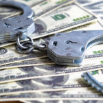 Handcuffs on a pile of one hundred dollar bills.