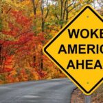 Yellow road sign: Woke America Ahead in autumn forest.