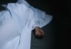 Hand emerging from under white sheet on dark surface.