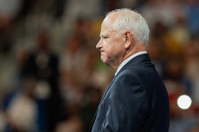 shutterstock_2499464649.jpg featured image Tim Walz in a suit standing before audience.