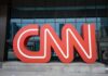 Red CNN logo in front of glass building.